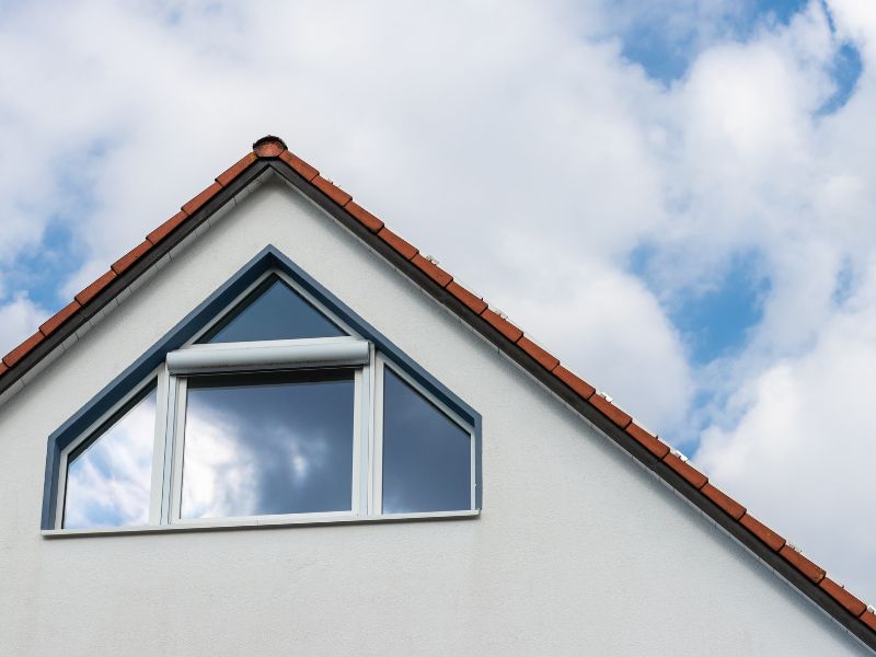 Großes dreieckiges Fenster an Hausfront mit außenliegenden Jalousien.