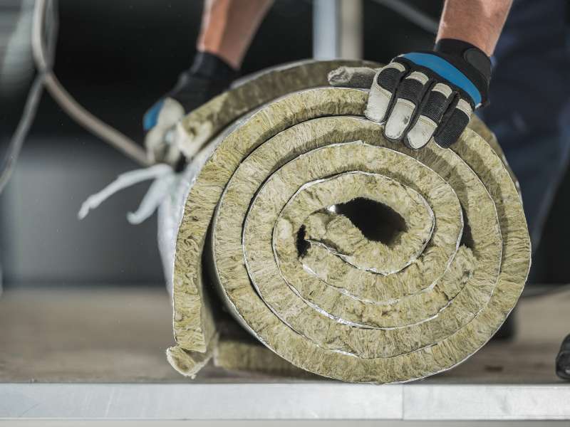 Bauarbeiter mit Arbeitshandschuhen verlegt eine Dämmrolle auf der Baustelle.