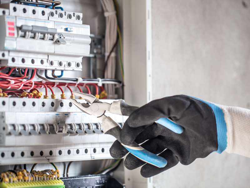 Hand mit Handschuh hält Zange an einem Stromkasten, Elektroinstallation im Einsatz.