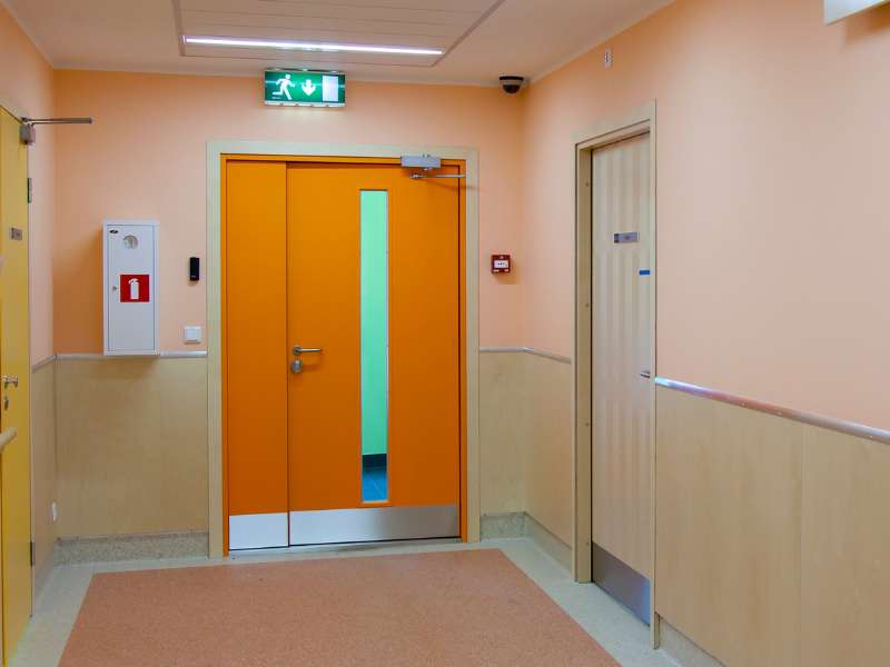 Tür in Krankenhausflur mit Sicherheitsvorgaben und barrierefreiem Zugang.