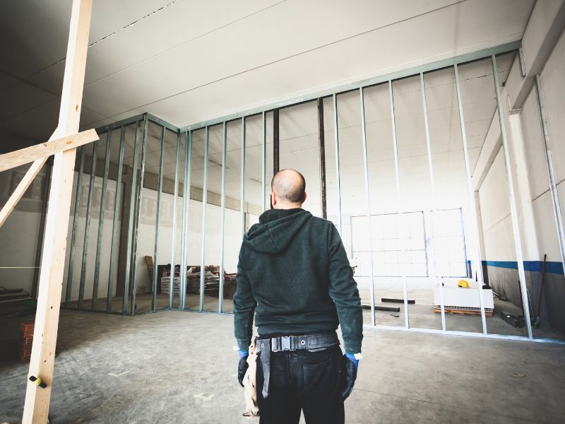Arbeiter geht auf eine hohe Metallständerwand zu, die für den Ladenbau im Gewerbe errichtet wurde.